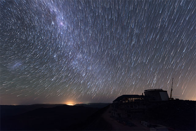 Vista nocturna del Observatorio Vera C. Rubin en construcción, las estrellas se ven como líneas curvas